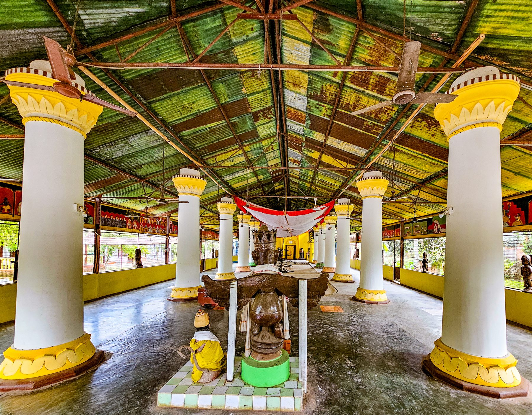 Open-sided prayer hall with white and yellow pillars and a small shrine