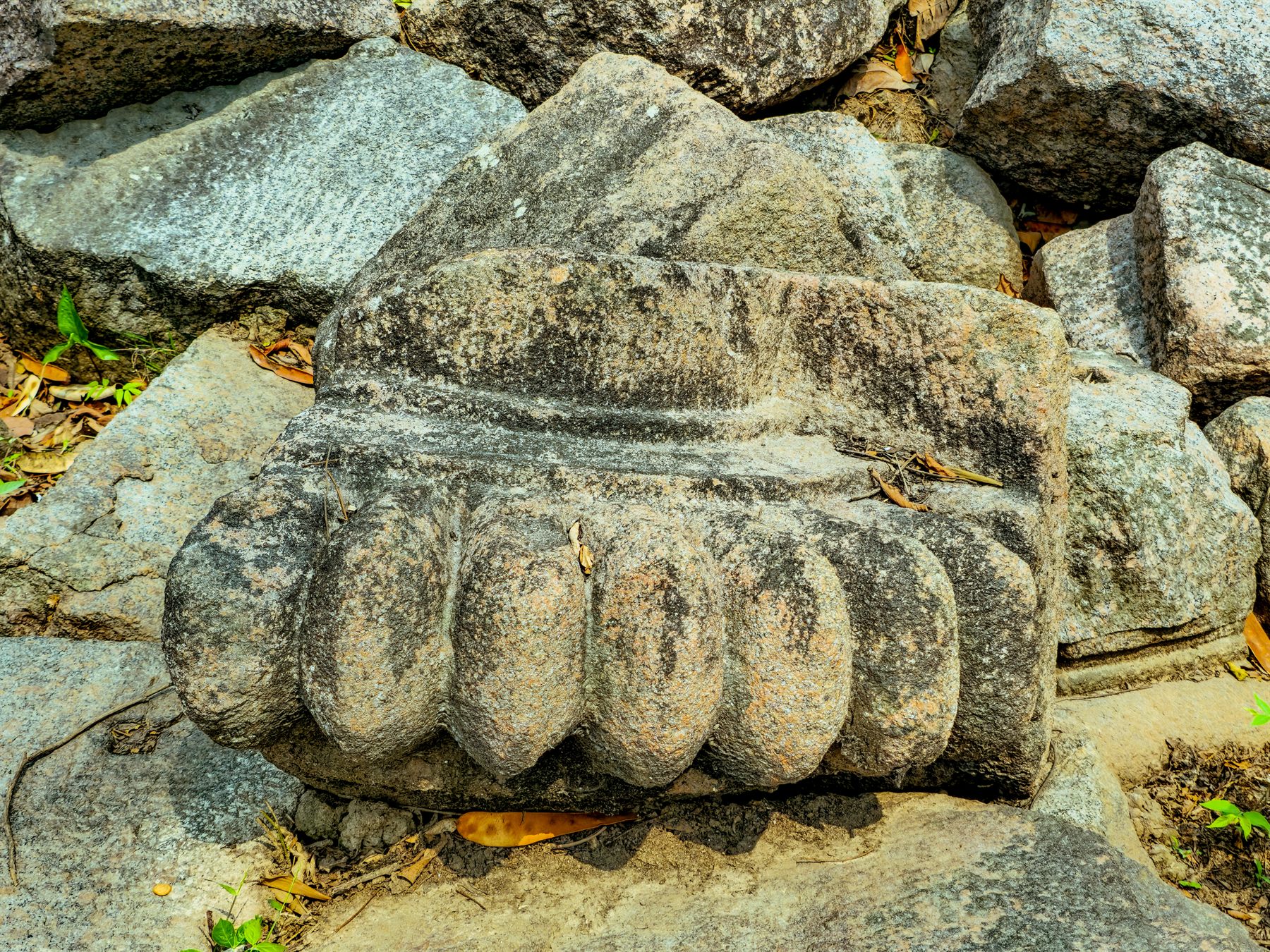 Close-up of a weathered carved stone fragment among fallen temple blocks